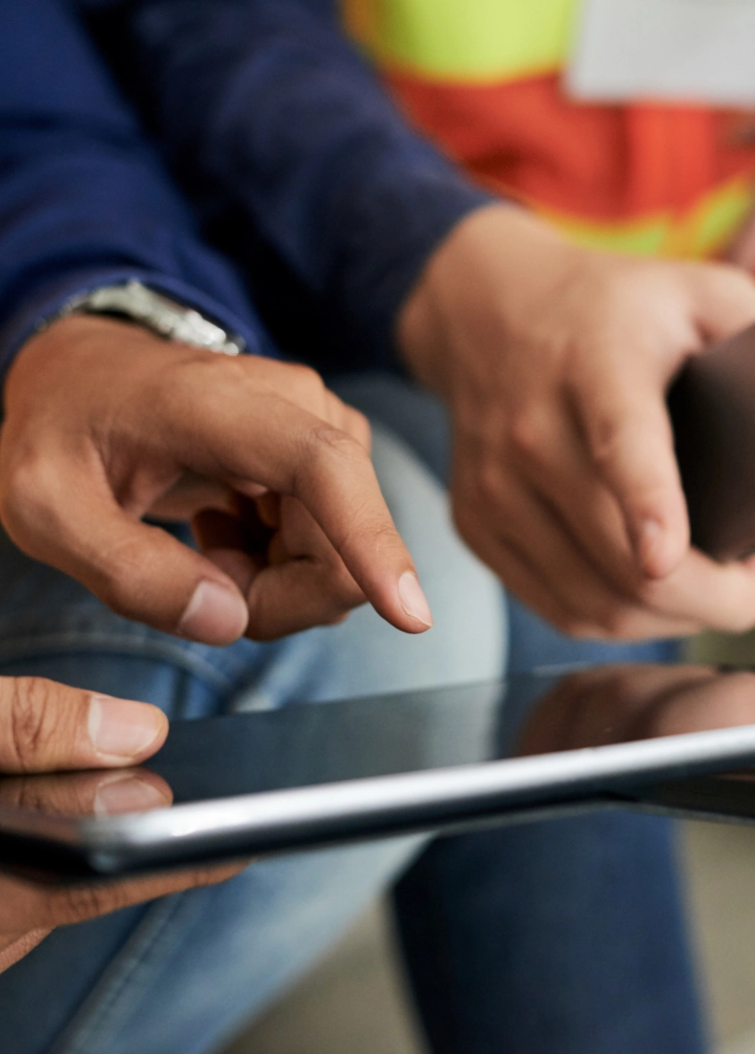 Two people closely viewing and interacting with a tablet screen, possibly discussing Emergency Septic Service. One person points at the screen while the other watches attentively.