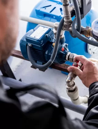 A person adjusts a valve on a network of pipes connected to a blue industrial machine, ensuring optimal performance for a septic system.