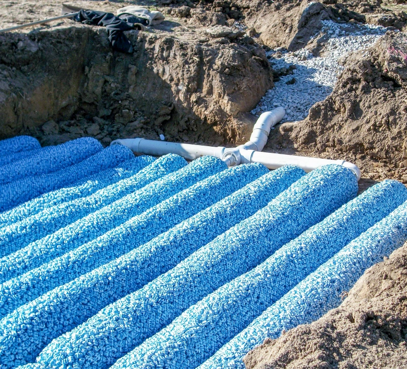 A construction site showing blue drainage pipes laid in parallel rows on a bed of gravel, surrounded by soil, expertly installed by a septic company.