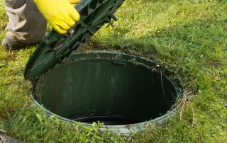 home septic service man opening manhole cover in backyard